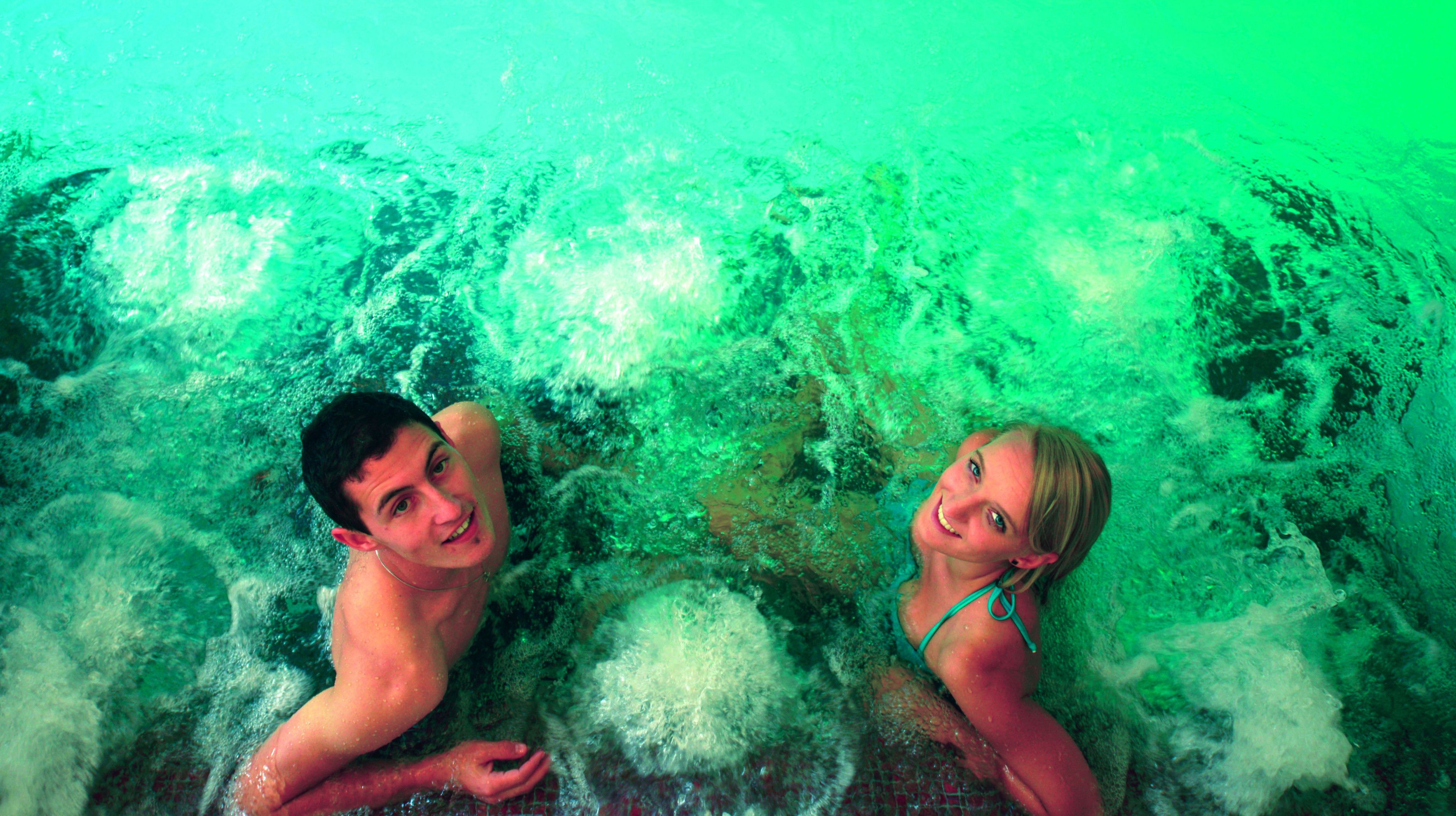 Two people in a water body with a greenish hue, surrounded by water.