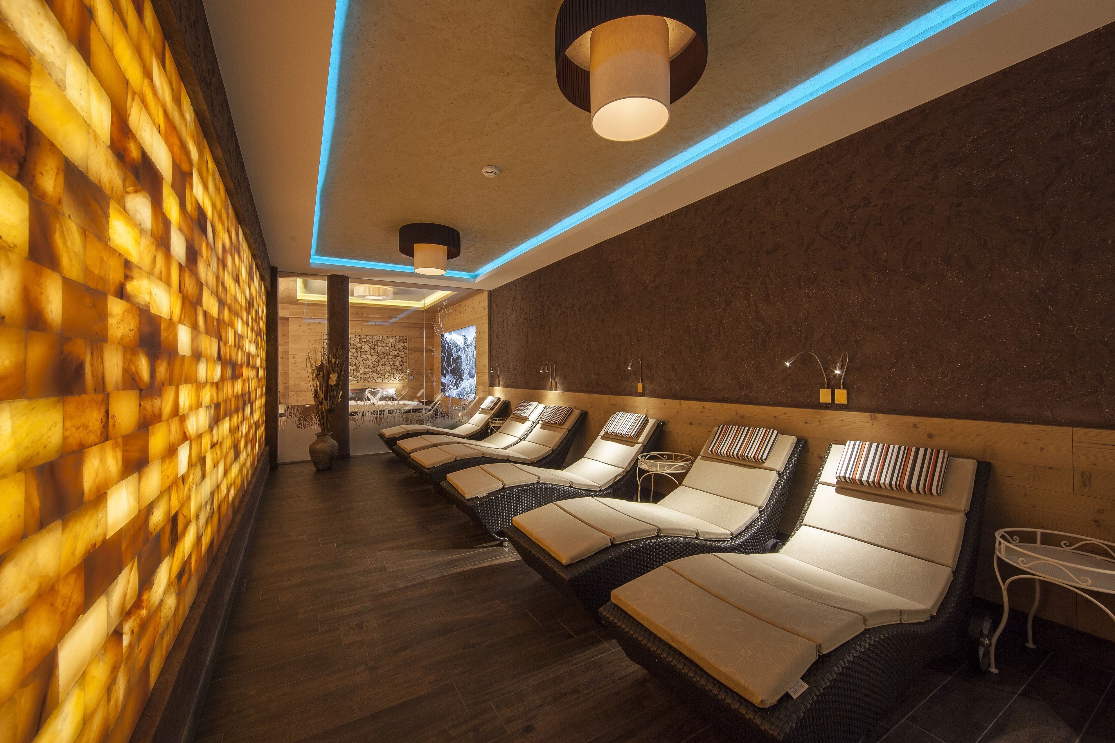 A spa room with wooden flooring, a brick wall, and multiple sun loungers with cushions.