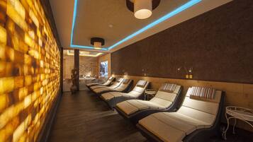 A spa room with wooden flooring, a brick wall, and multiple sun loungers with cushions.