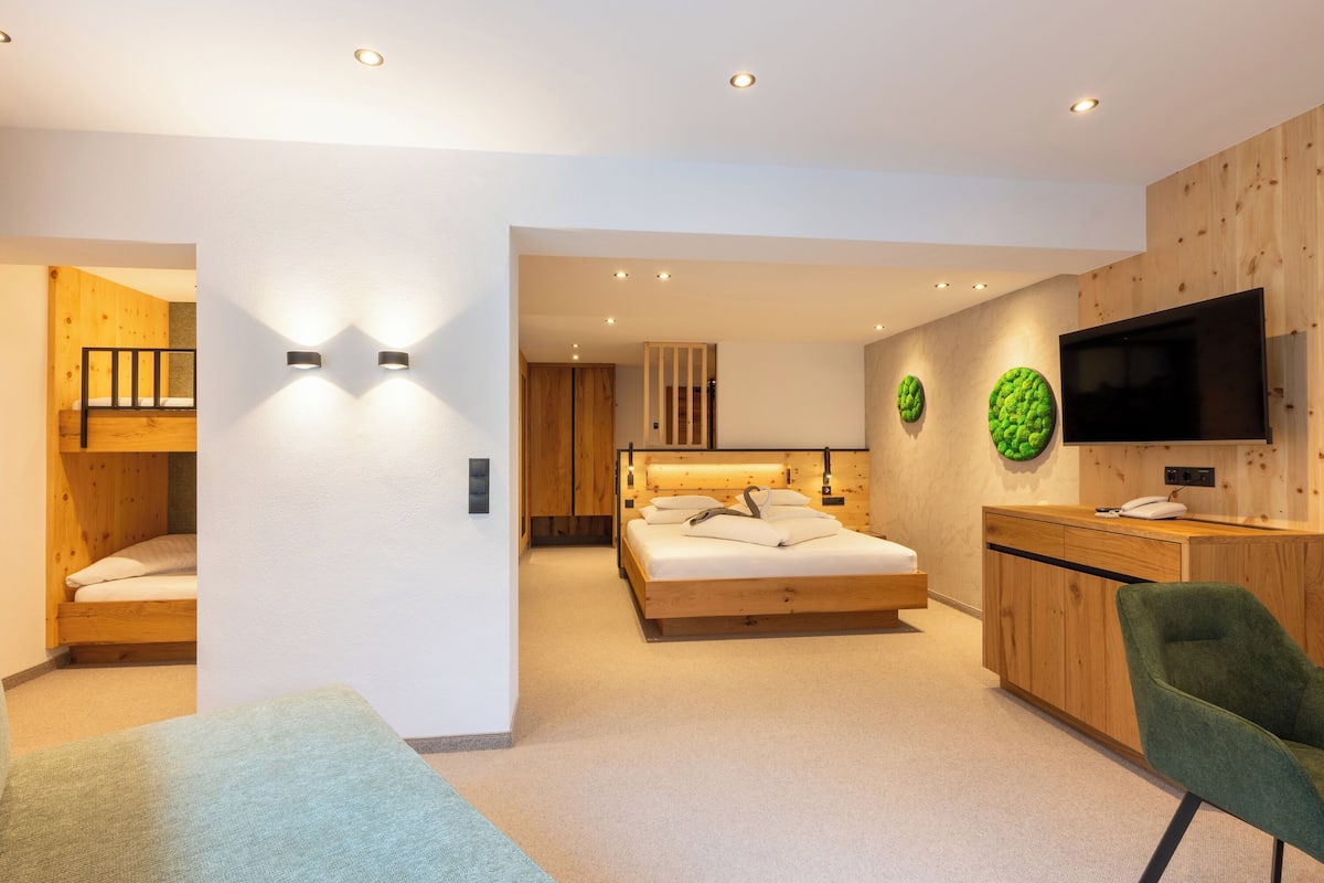Un dormitorio moderno con una litera, una cama individual, un escritorio con una silla y un televisor montado en la pared.