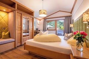 A bedroom with a bed, wooden wardrobe, and a window with a view of greenery. - Hotel Jäger (Tux)