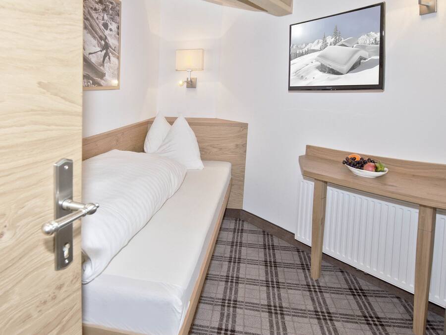 Une chambre à coucher avec un lit, une table de chevet sur laquelle se trouve un bol de fruits, une lampe fixée au mur et un tableau encadré.