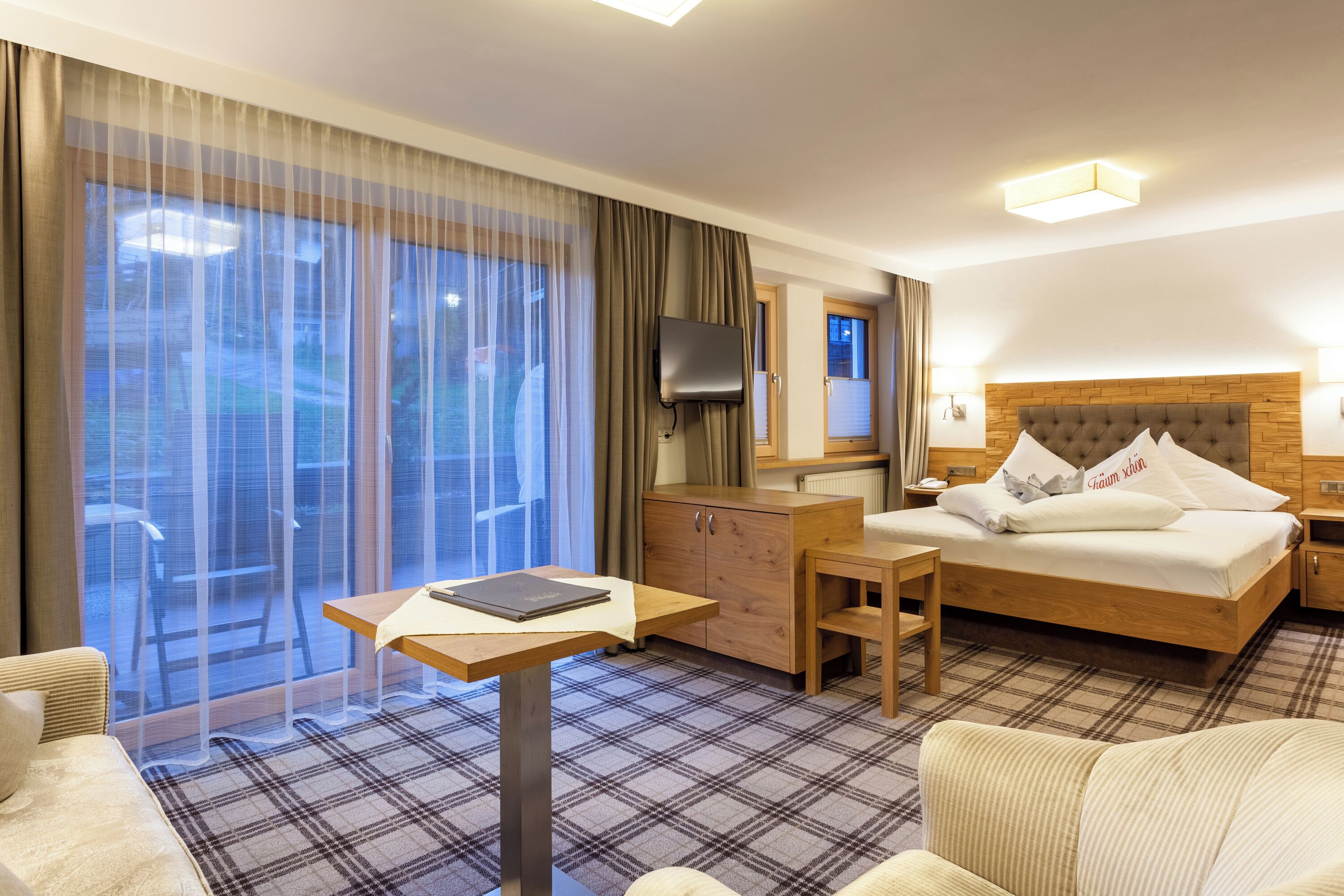 A hotel room with a bed, a desk, a chair, a television, and a view through large windows.