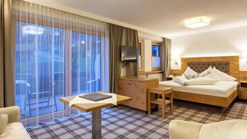 A hotel room with a bed, a desk, a chair, a television, and a view through large windows.