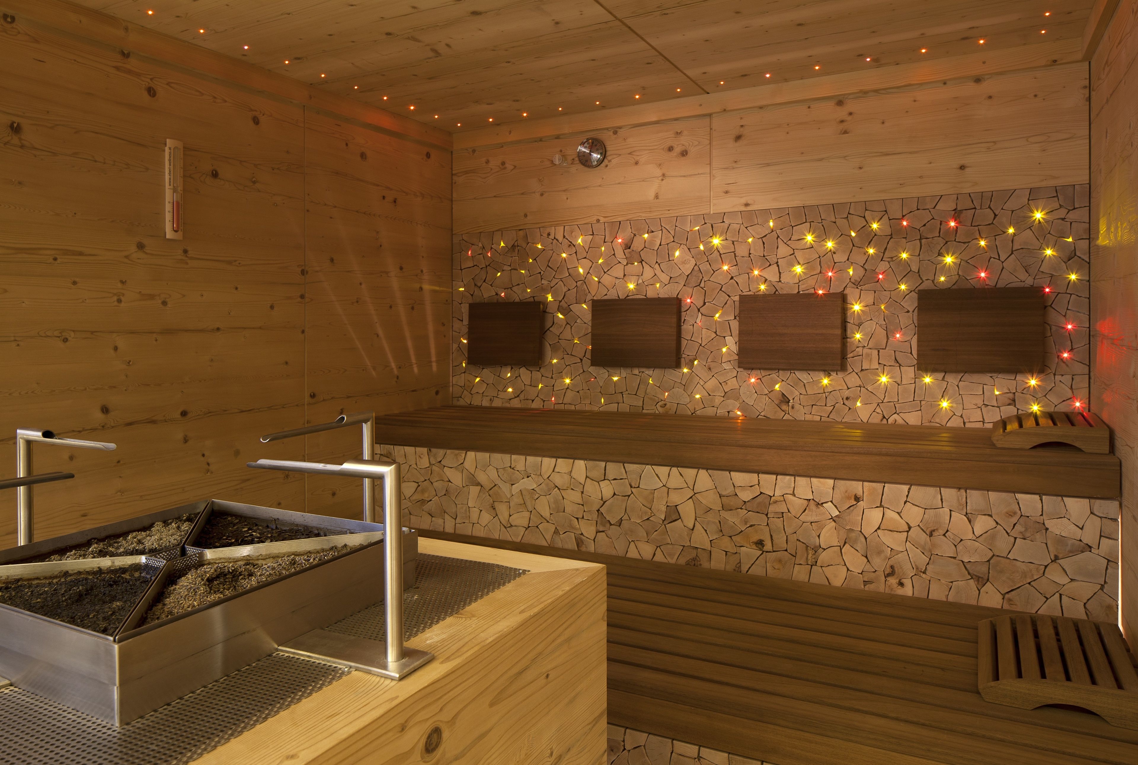 A sauna with wooden walls, a stone mosaic wall, and three wooden benches.