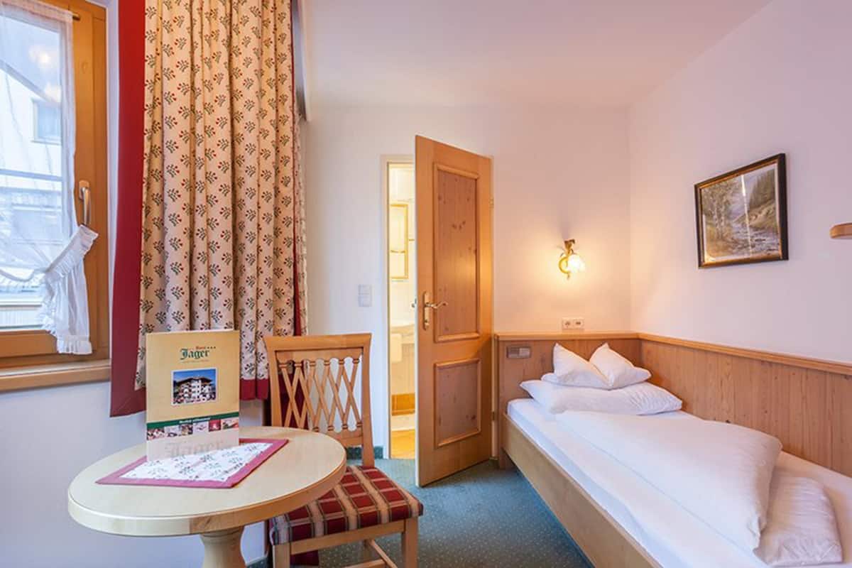 Una habitación de hotel con una cama, una mesa con un menú, una silla, una puerta y un cuadro en la pared.