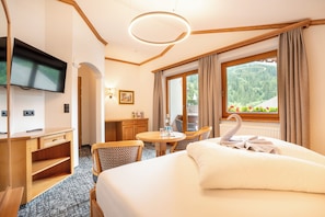 A hotel room with a bed, a desk, a chair, a table, a TV, and a window with curtains. - Hotel Jäger (Tux)