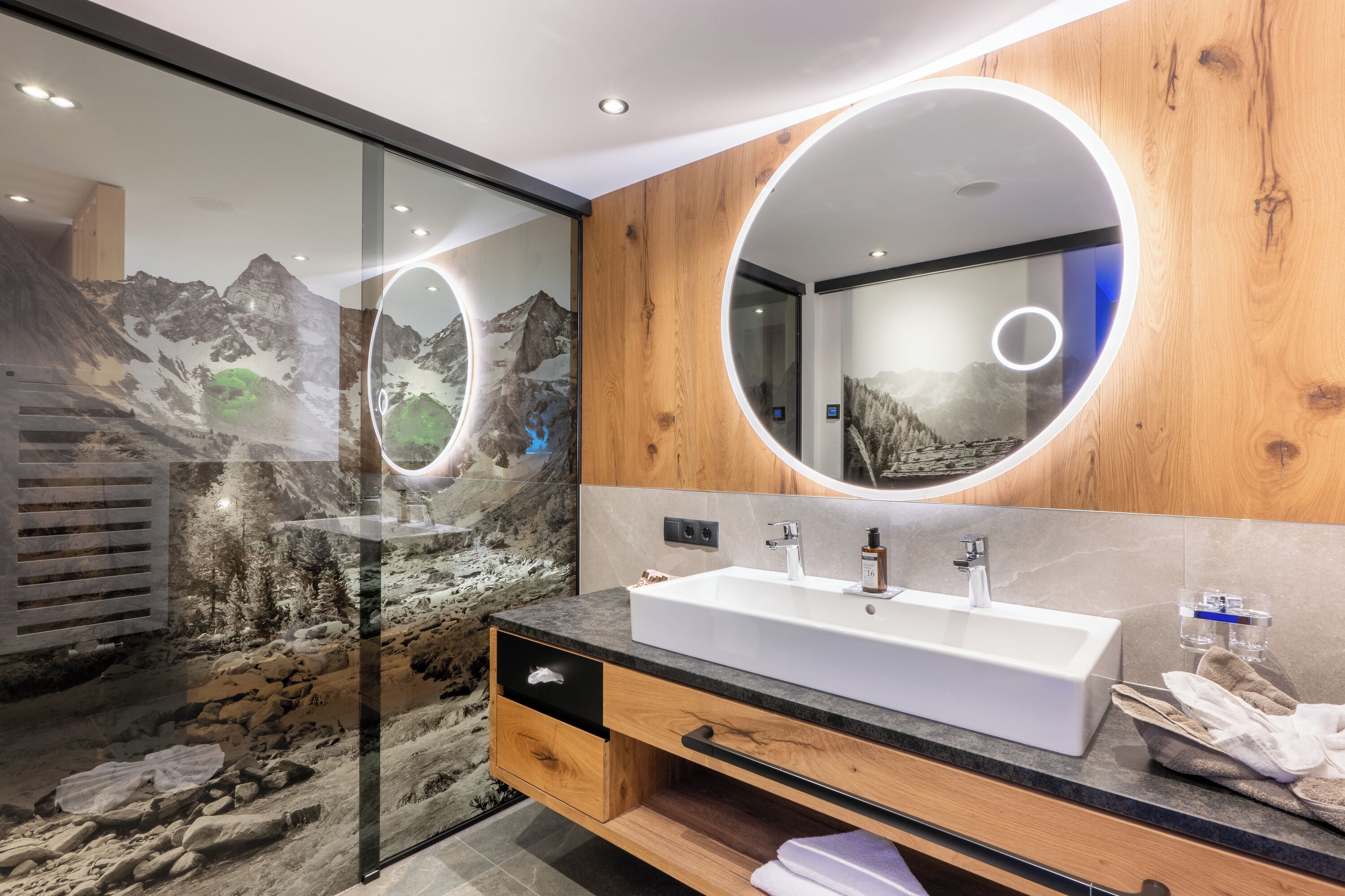 A modern bathroom with a large mirror, wooden paneling, a white sink, and a glass shower enclosure.