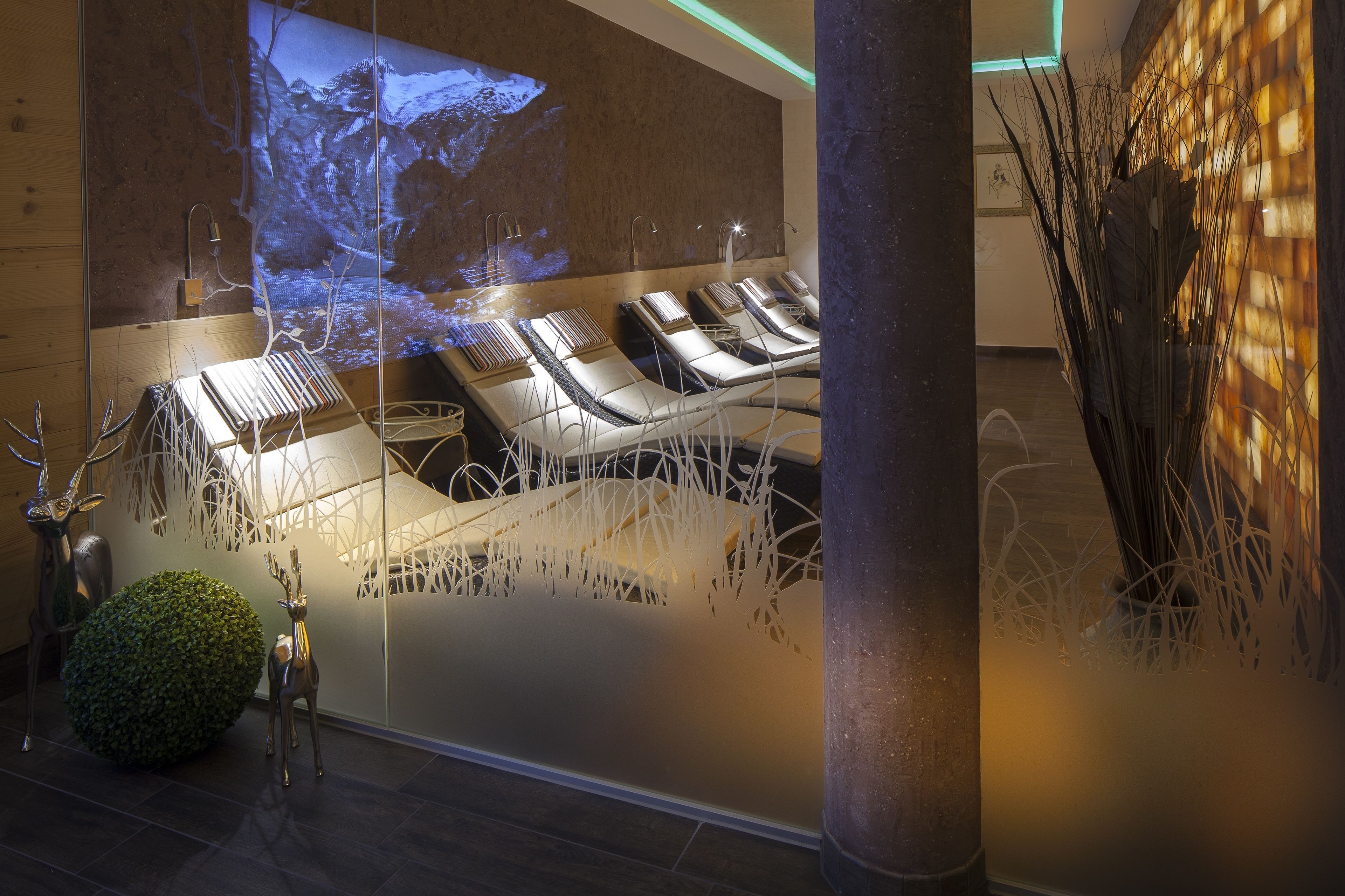 Un espace de détente avec des fauteuils inclinables, un écran de projection diffusant des images de la nature, et des éléments décoratifs tels qu’un petit arbre et des sculptures abstraites.