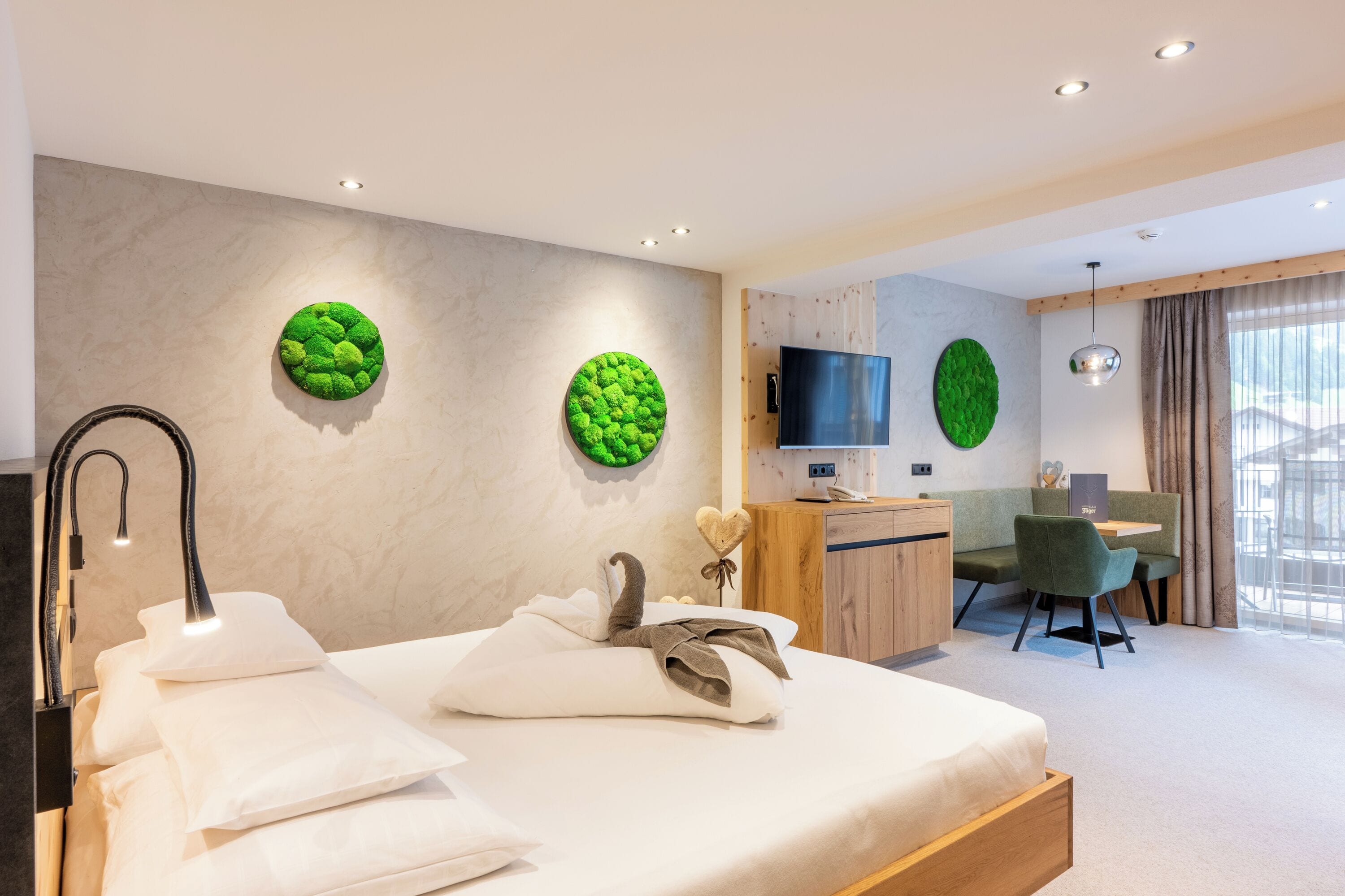 A modern hotel room with a bed, a desk, a TV, and a green wall decoration.