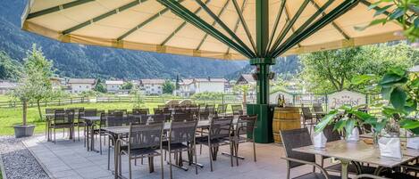 An outdoor patio with tables and chairs, a large umbrella, and a view of a mountain and buildings in the background.