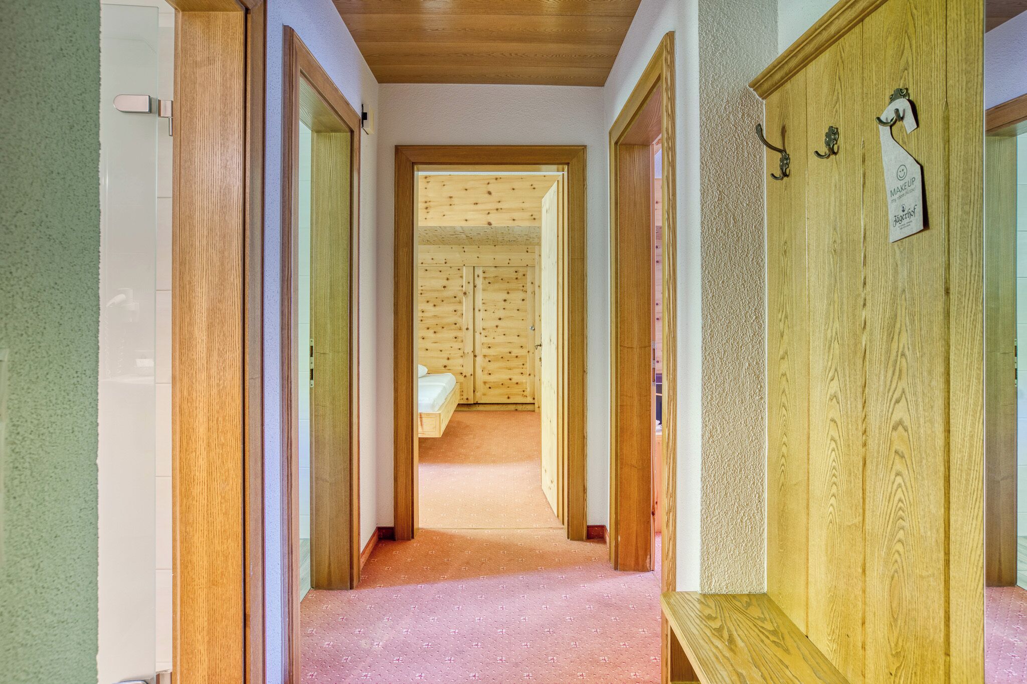 Un couloir avec des portes en bois menant à une pièce où se trouve un lit.