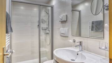 Un baño moderno con ducha de vidrio, lavabo blanco y un espejo grande.