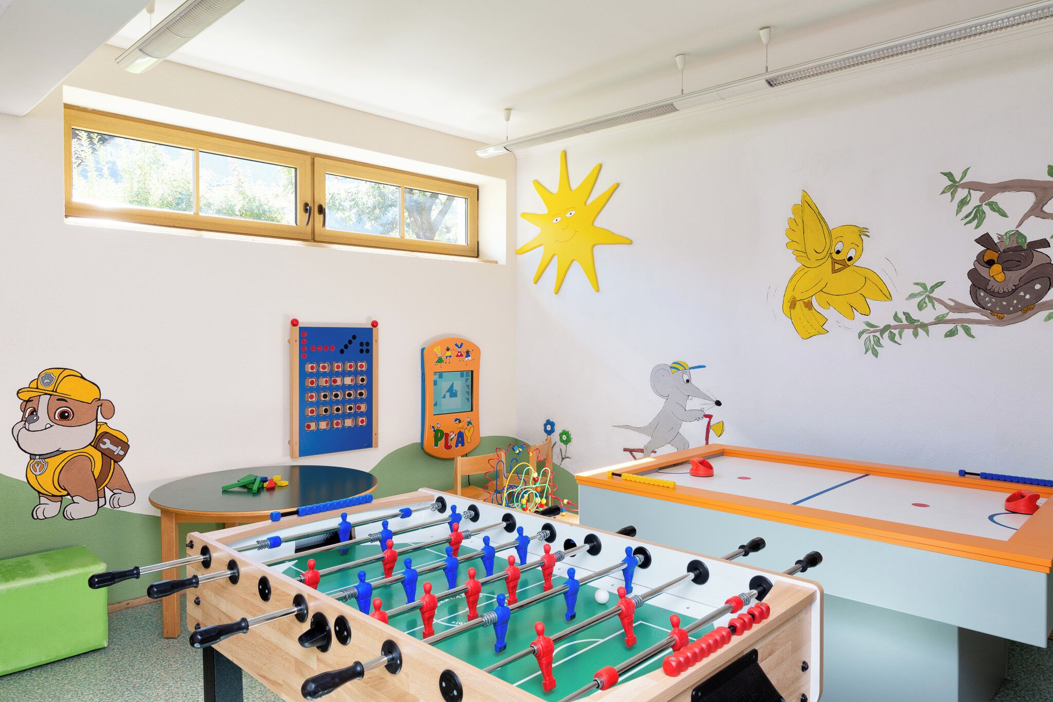 A children's playroom with two foosball tables, educational toys, and playful wall decorations.