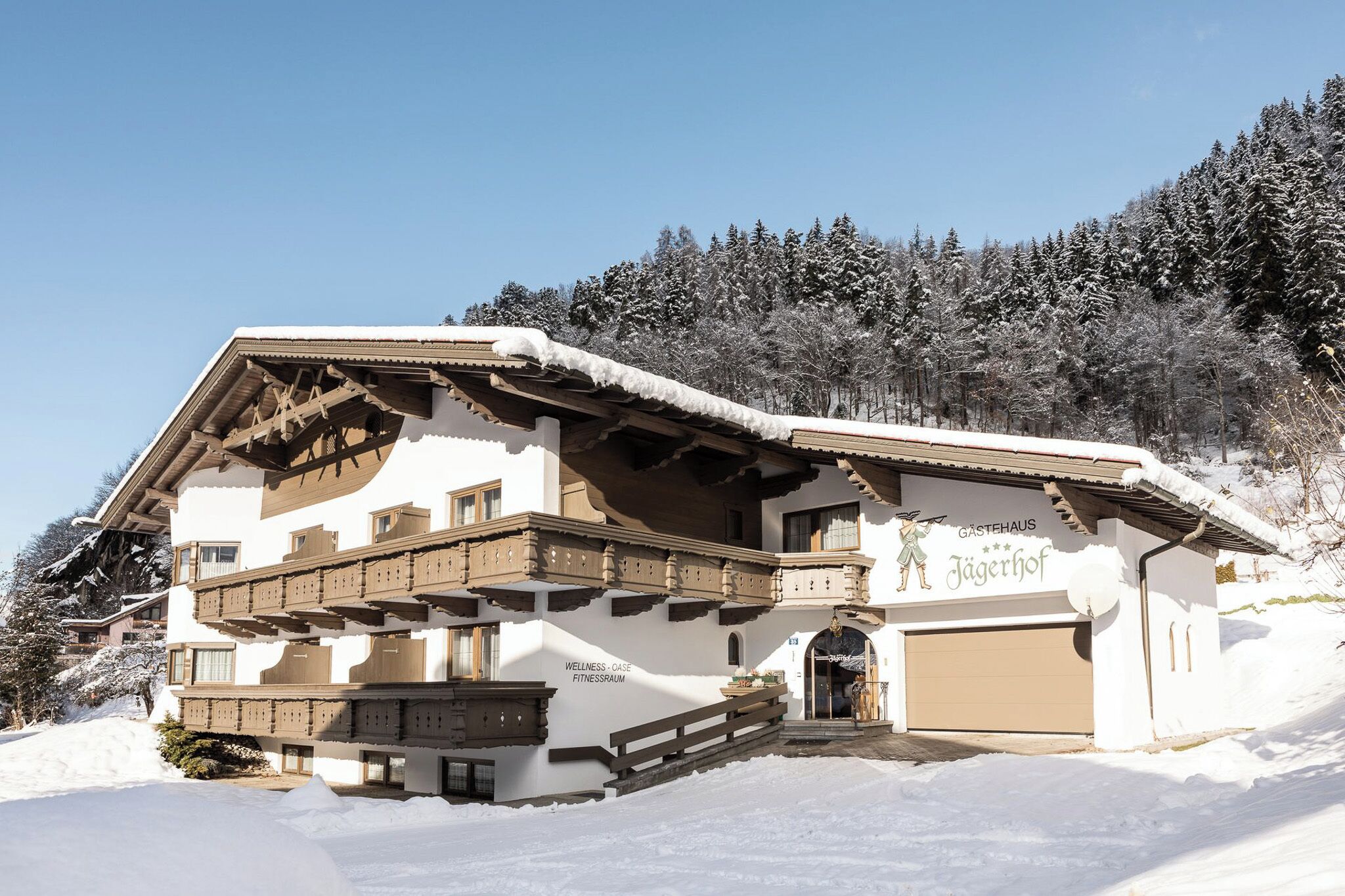 A multi-story building with a snow-covered roof, balconies, and a sign that reads "Gästehaus Jägerhof".