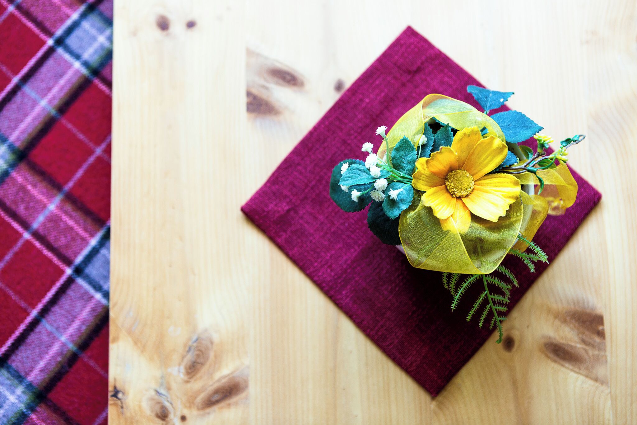 Una superficie de madera con un paño morado y un arreglo floral.