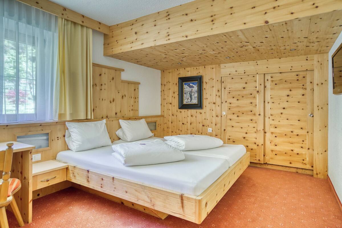 A wooden room with a bed, a desk, and a window with curtains.