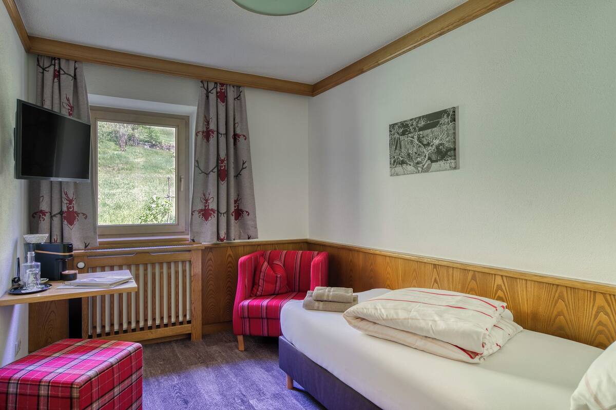 A bedroom with a bed, a desk with a TV, a chair, and a radiator.