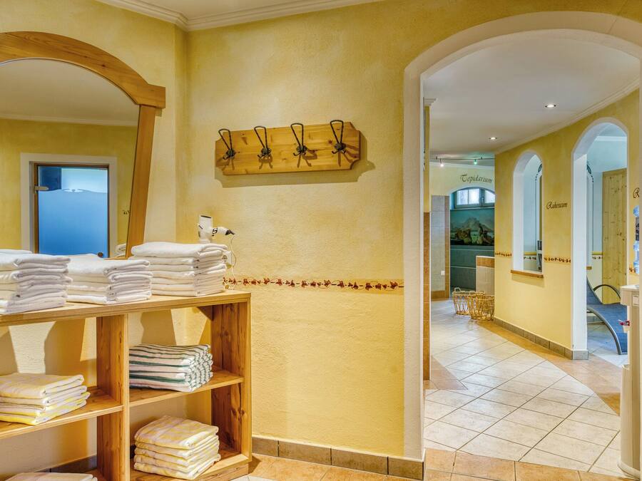 Un baño de hotel con un estante de madera con toallas, un toallero de madera montado en la pared y un espejo.