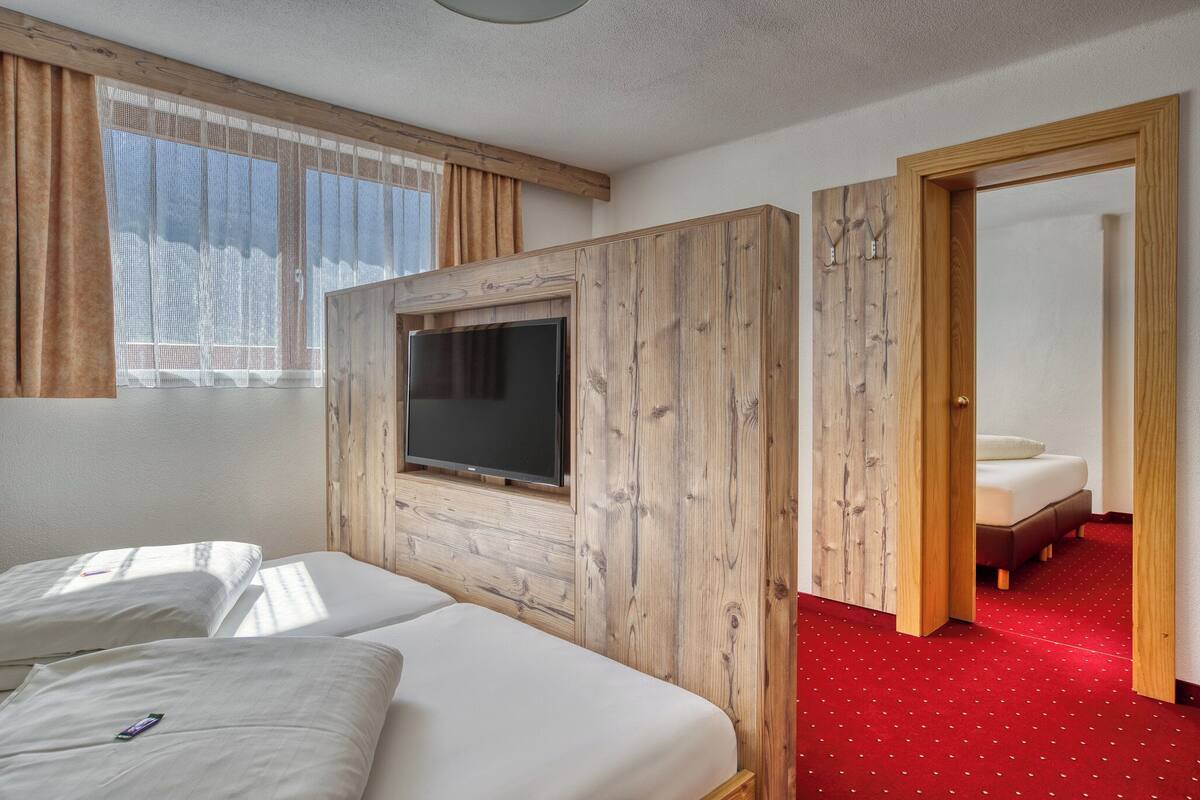 A hotel room with a wooden wardrobe, a TV mounted on the wall, and a red carpeted floor.
