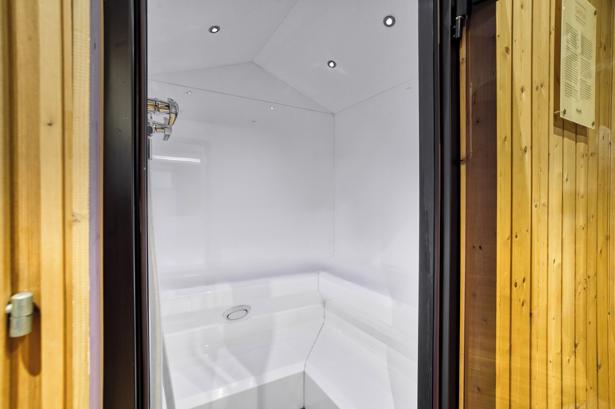 A modern bathroom with a glass shower enclosure, a visible showerhead, and a wooden wall panel.