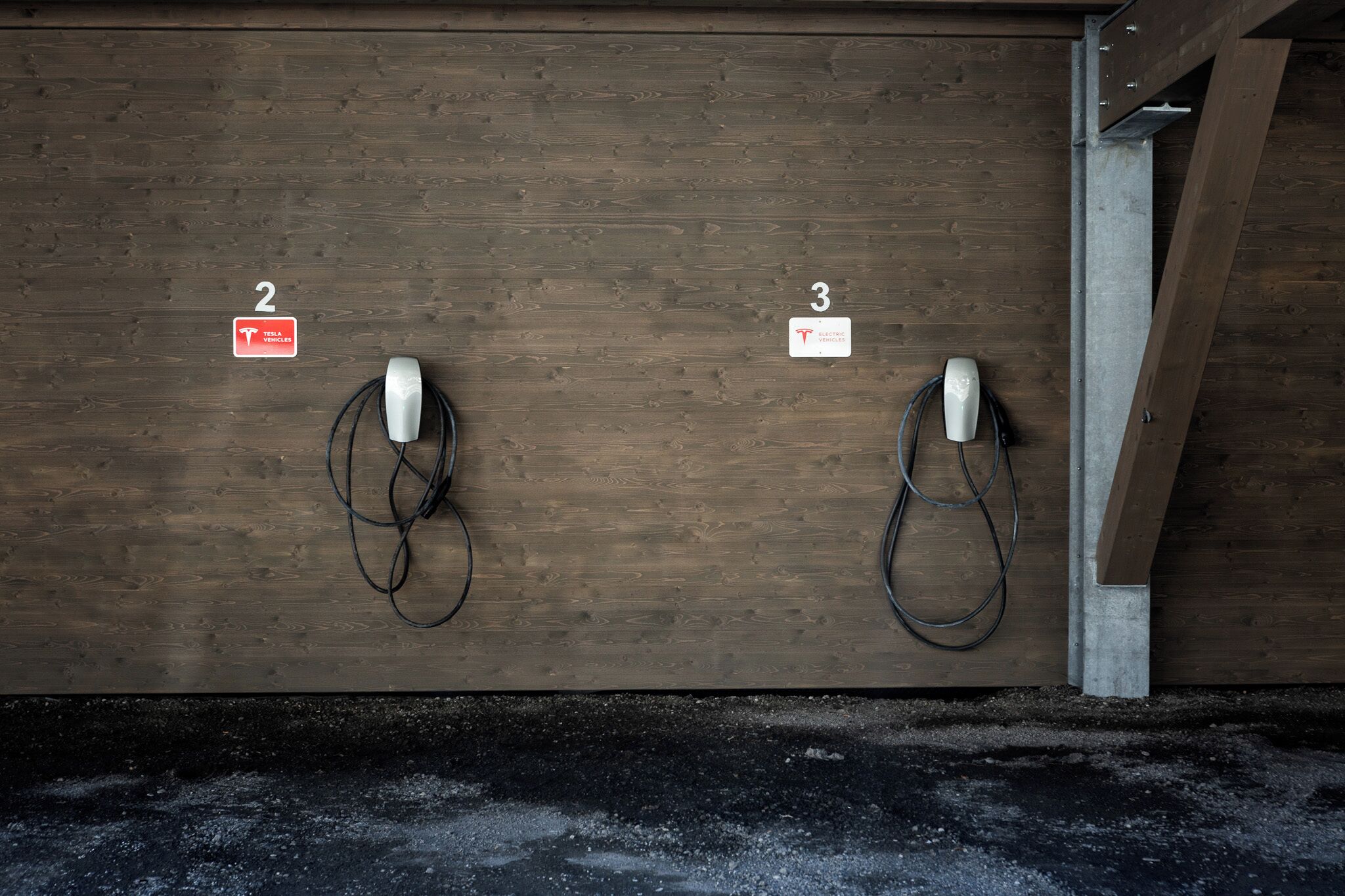 Dos estaciones de carga para vehículos eléctricos, identificadas con los números 2 y 3, en una pared de madera.