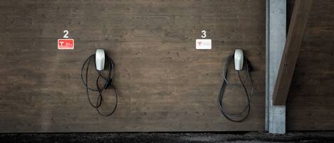 Dos estaciones de carga para vehículos eléctricos, identificadas con los números 2 y 3, en una pared de madera.
