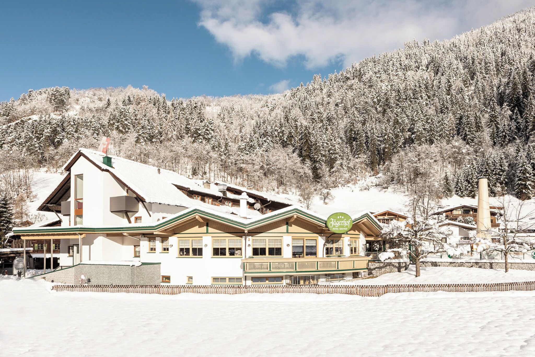 A traditional alpine-style building with a sloped roof, large windows, and a sign indicating it is a hotel.