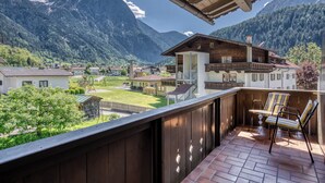 Ein Balkon mit Holzbalkonen, der auf eine gebirgige Landschaft blickt, ein Holzhaus mit Balkon und ein klarer Himmel.
