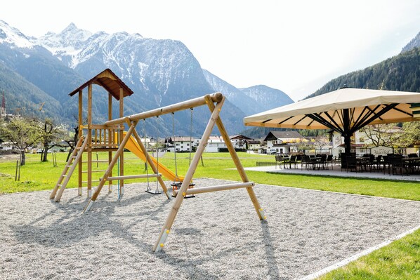 A playground with a swing set and slide, surrounded by a park with a mountain backdrop. - Hotel Jägerhof (Oetz)