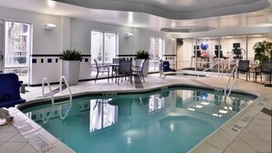 An indoor swimming pool with clear water, surrounded by seating areas and potted plants.