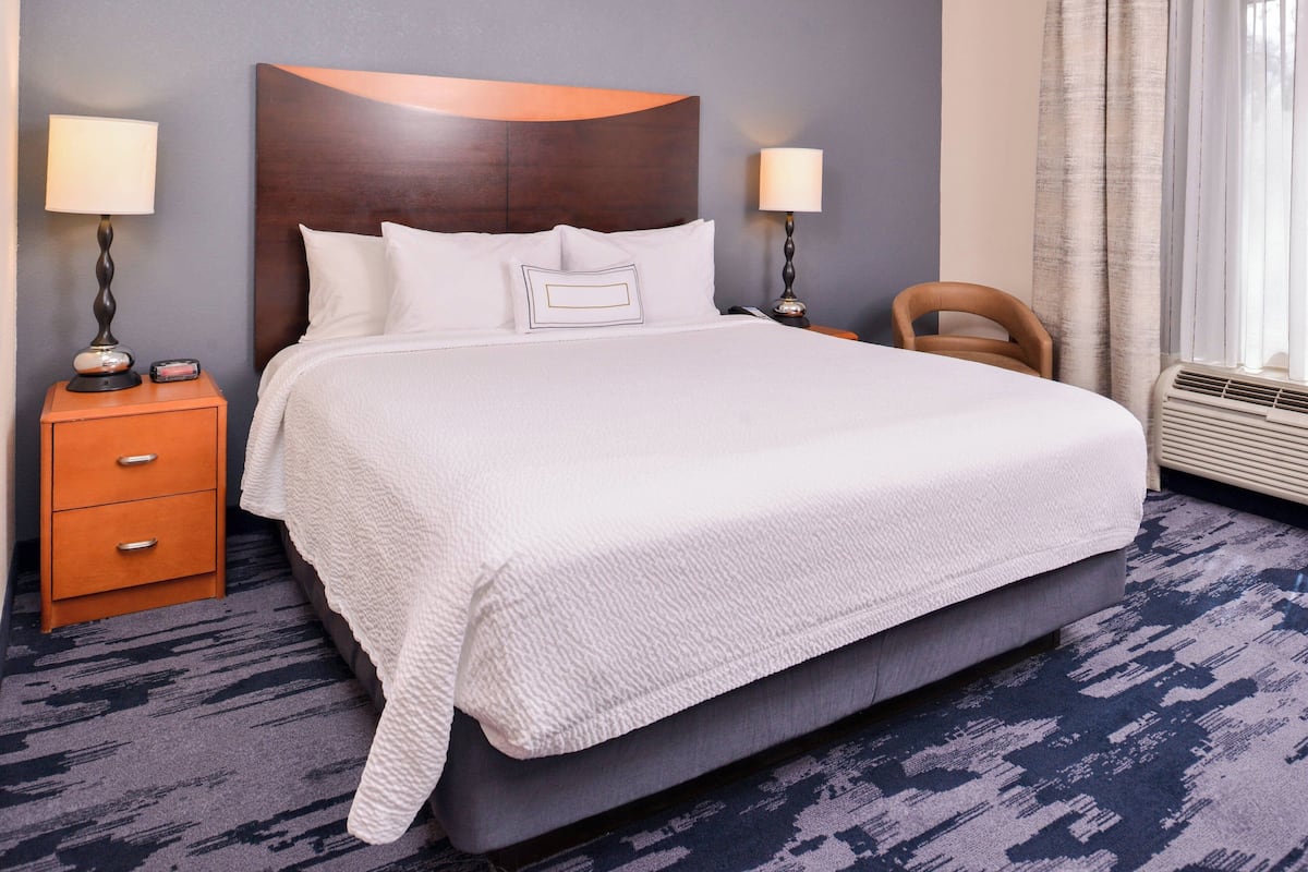 A neatly made bed with white linens, a wooden headboard, and a nightstand with a lamp.