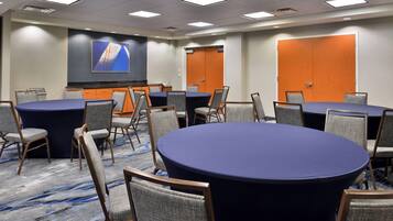 Une salle de conférence équipée de tables rondes, de chaises, d’un écran de projection et d’un sol recouvert de moquette.
