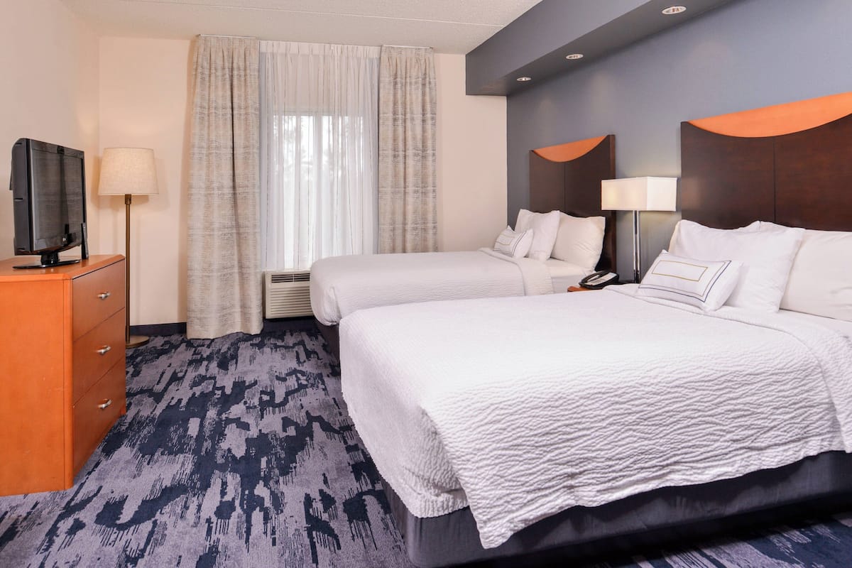 A hotel room with a large bed, a TV on a wooden dresser, and a window with curtains.