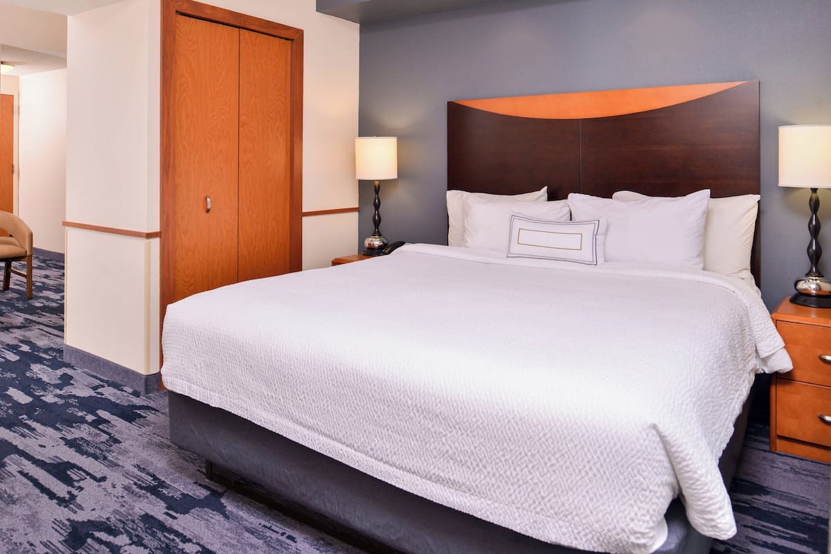 A hotel room with a large bed, two bedside tables with lamps, a wooden wardrobe, and a carpeted floor.