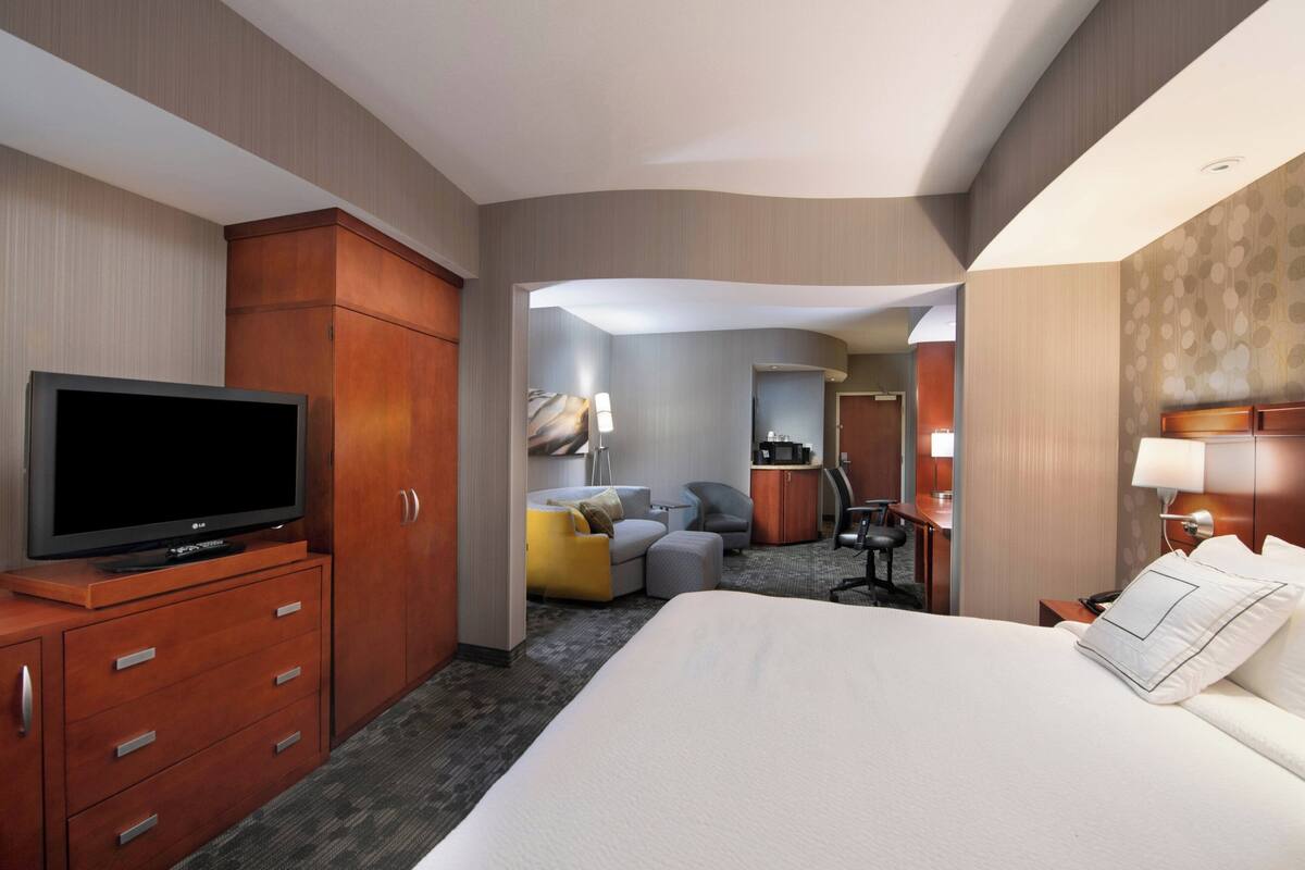 Een hotelkamer met een groot bed, een televisie op een houten kast, een bureau met stoel, een bank en een kleine kitchenette.