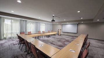 A conference room with a long table, chairs, a projector screen, and a carpeted floor.
