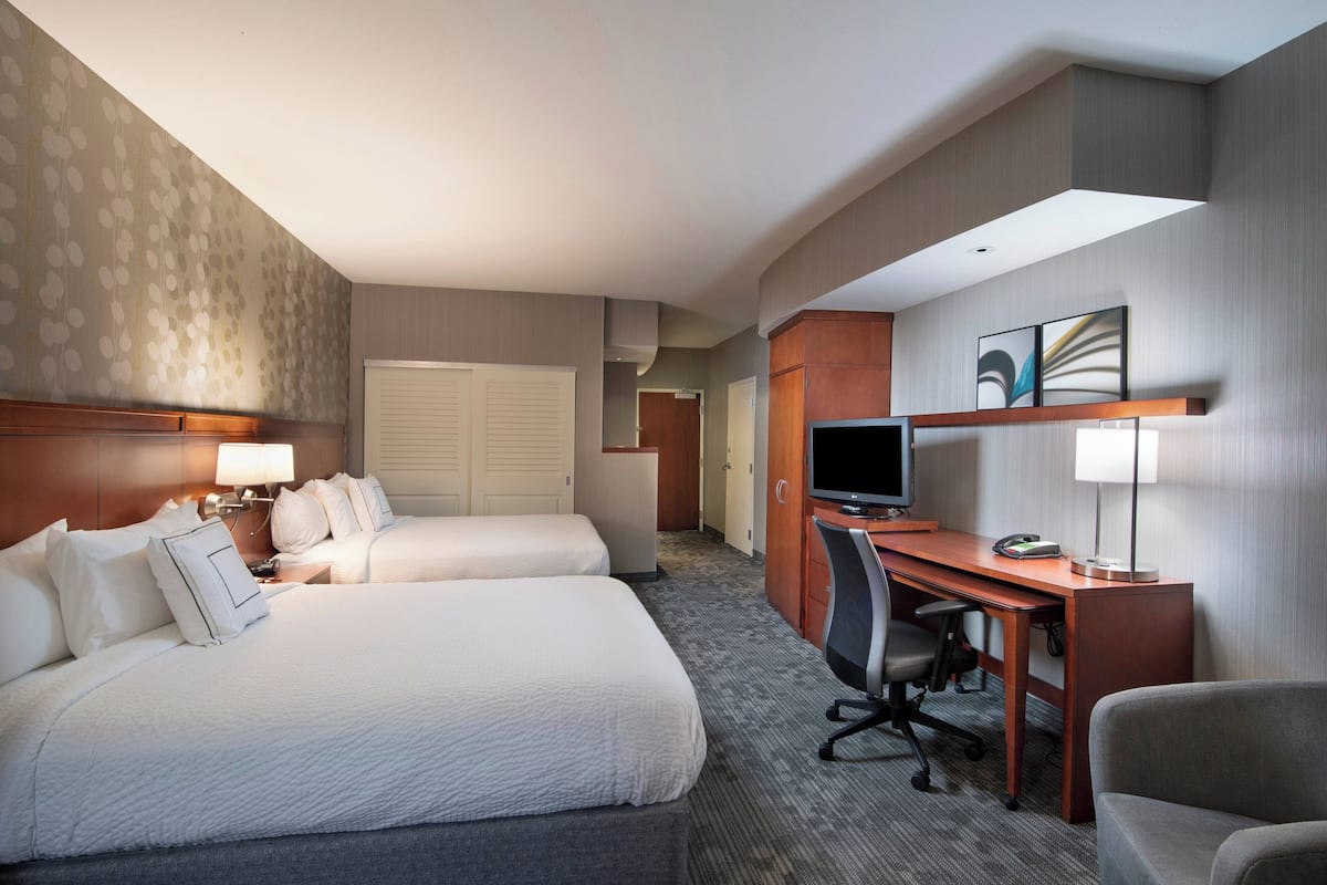Een hotelkamer met twee bedden, een bureau, een stoel, een televisie en een lamp.