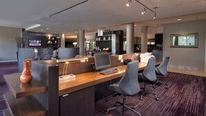 Un espace de bureau moderne avec un grand bureau en bois, plusieurs chaises, un téléviseur et un coin cuisine à l’arrière-plan.