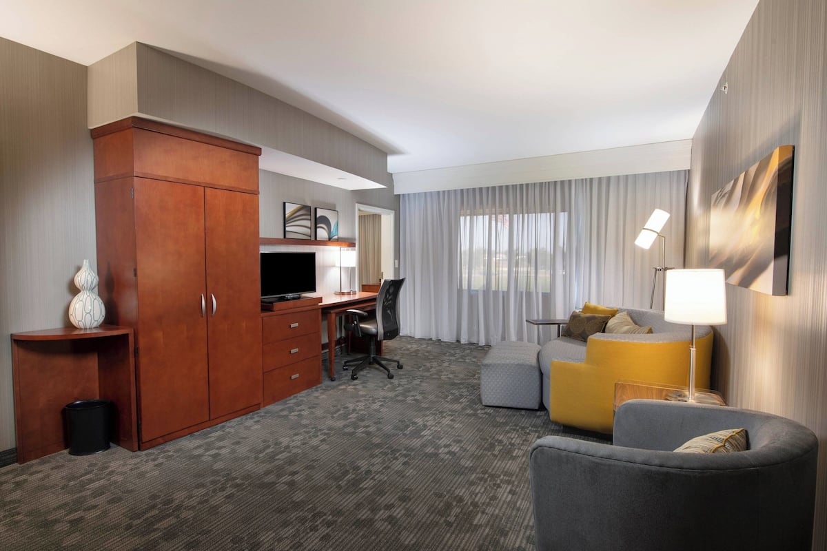 Een hotelkamer met een houten garderobe, een bureau met stoel, een bank, een televisie en een lamp.