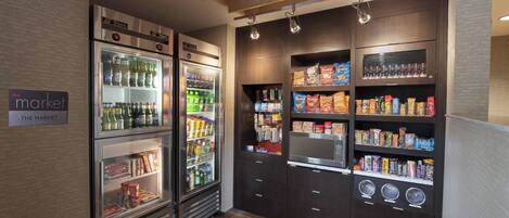 Zona de venta automática de bebidas y aperitivos con diversas opciones refrigeradas y no refrigeradas, que incluye un microondas y una máquina de café.