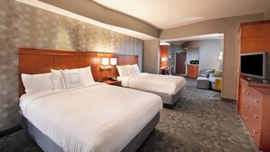 Une chambre d’hôtel avec deux lits, un bureau, une télévision et une salle de bain visible au fond.