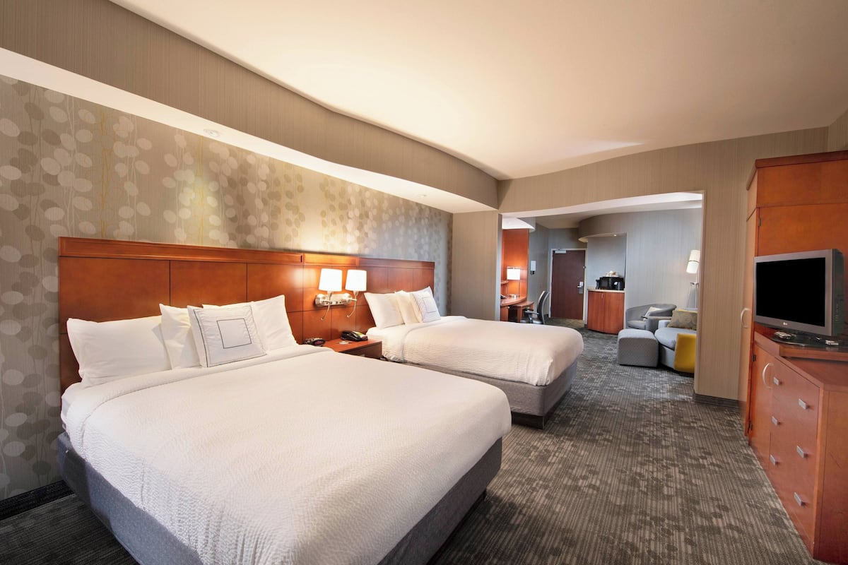 Een hotelkamer met twee bedden, een bureau, een televisie en een badkamer in de achtergrond.