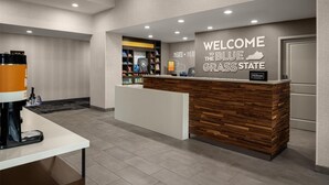 Un área de recepción con un mostrador de madera, una máquina de café y un cartel que da la bienvenida a Blue Grass State.