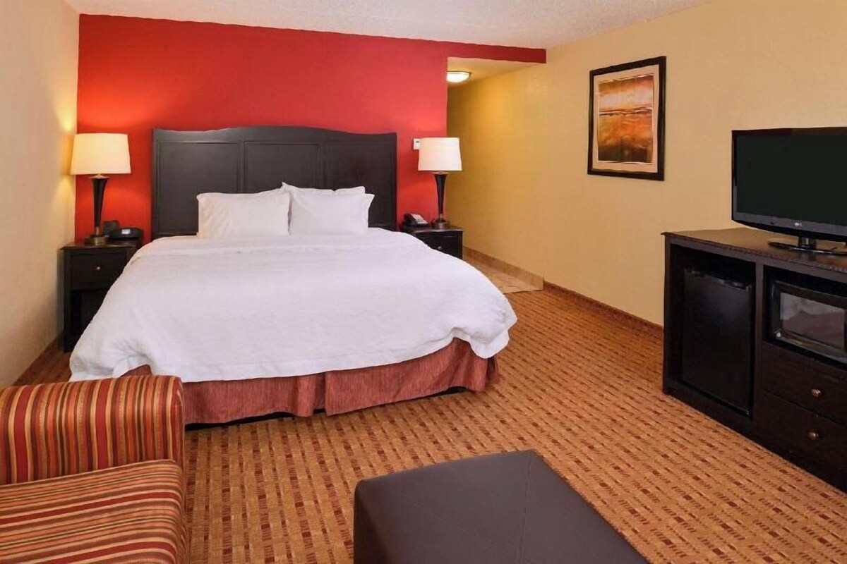 A hotel room with a large bed, two bedside tables with lamps, a television, and a framed picture on the wall.