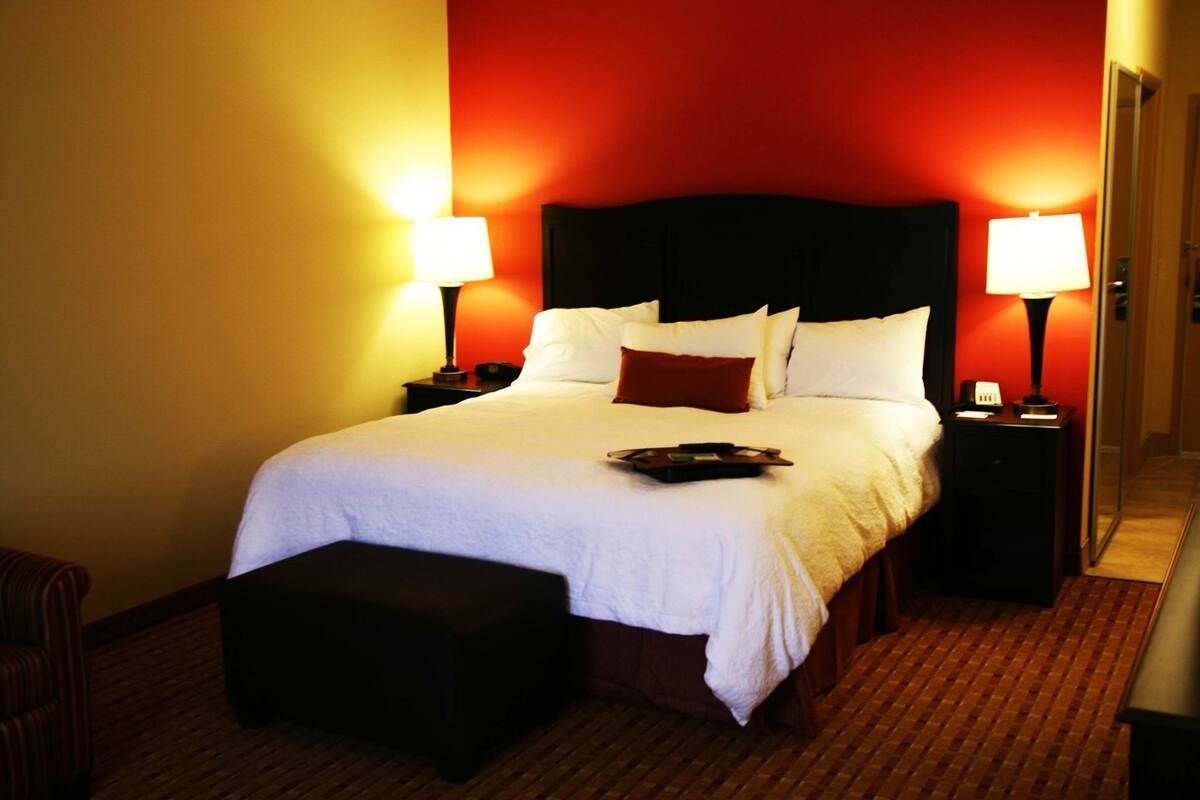 Ein Hotelzimmer mit einem großen Bett, zwei Nachttischen mit Lampen, einer hölzernen Bank und einer roten Akzentwand.