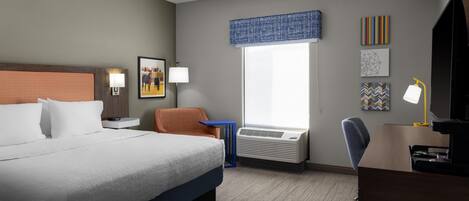 Ein Hotelzimmer mit einem Bett, einem Schreibtisch, einem Stuhl, einem Fenster mit Jalousien und einer Wandklimaanlage.
