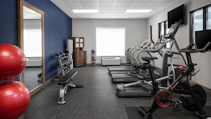 Un gimnasio con cintas de correr, elípticas y balones de ejercicios rojos.