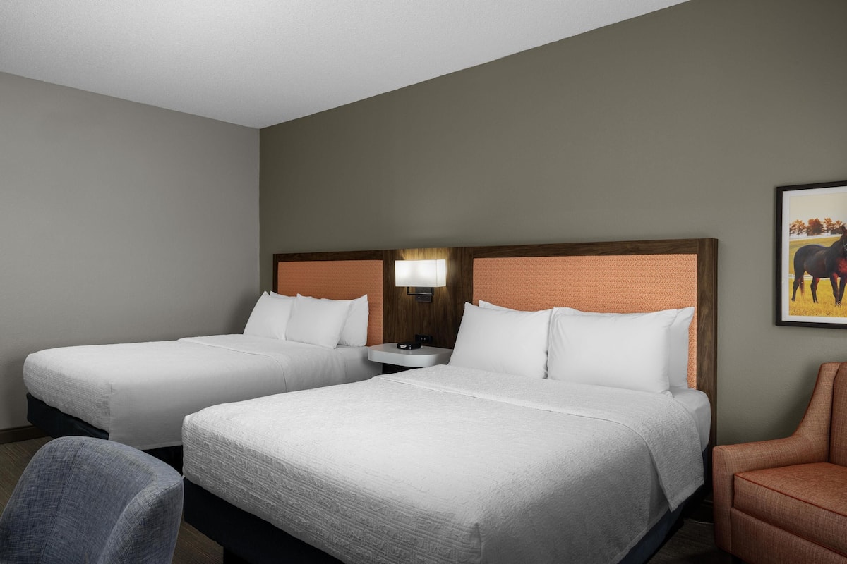 Ein Hotelzimmer mit zwei Betten, einem kleinen Tisch, einem Stuhl und einem Gemälde an der Wand.