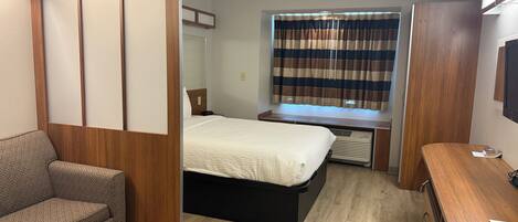 A compact hotel room with a bed, a desk, a chair, and a small sofa.